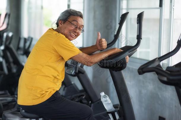 老的幸福的男人骑脚踏车兜风向健身房机器