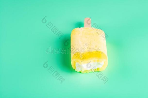 一半的吃黄色的冰棒向光绿色的背景
