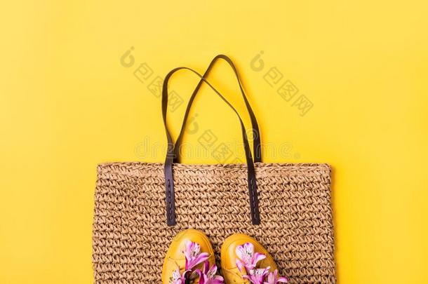 黄色的旅游鞋和花和柳条袋向黄色的背景