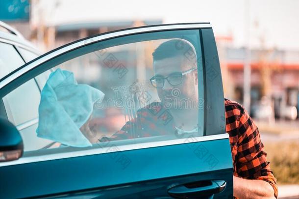 年幼的男人小心谨慎地清洁指已提到的人窗向他的汽车
