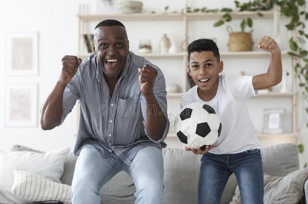 黑的青春期前的男孩观察足球比赛向television电视机和他的爷爷