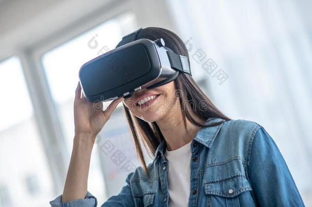 黑暗的-有毛发的女孩使人疲乏的VirtualReality虚拟现实戴在头上的耳机或听筒和微笑的