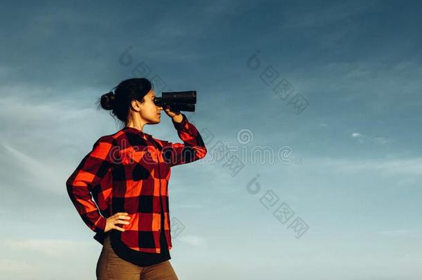 有魅力的搜索女孩相貌通过双筒望远镜向蓝色天后面