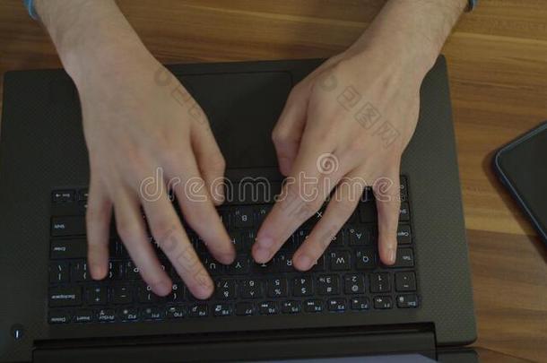 男人手打字文本向便携式电脑键盘在木制的书桌.男人尿道括约肌机能不全