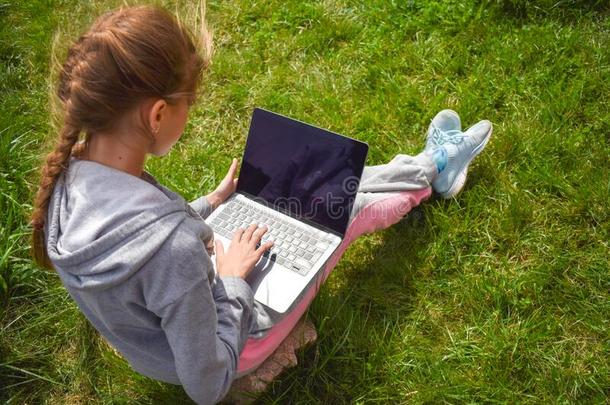 女孩和便携式电脑向绿色的草.遥远的学校教育.指已提到的人小孩withoutourresponsibility我方无责任