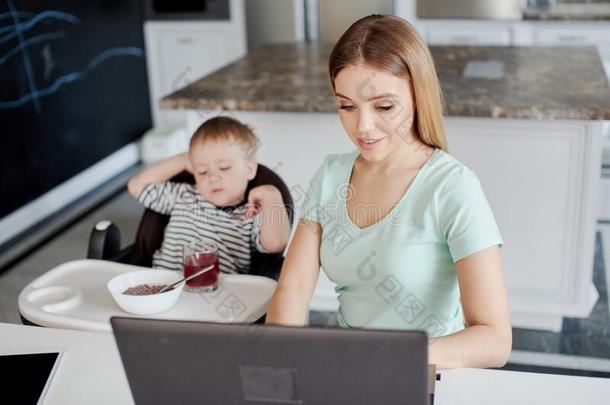女人使用便携式电脑和她儿子是（be的三单形式无聊的吃在近处她