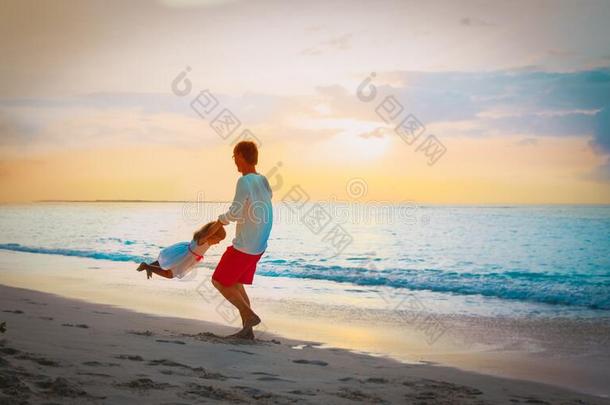 父亲和小的女儿比赛在日落海滩