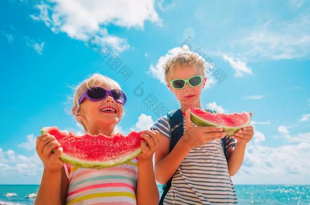 幸福的男孩和女孩吃西瓜在海滩,健康的生活方式