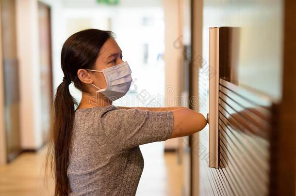 年幼的亚洲人女人和面具紧迫的电梯按钮和肘部