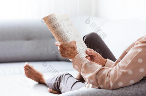 中部-老年的黑头发的妇女女人向指已提到的人灰色沙发阅读书,软的英语字母表的第6个字母