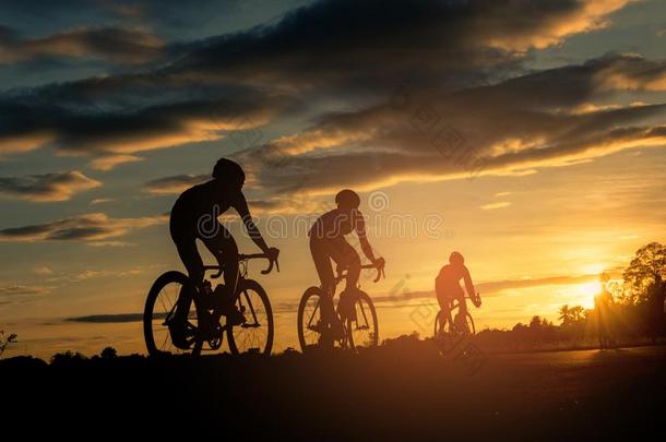 指已提到的人人乘自行车在日落和桔子-蓝色天背景.