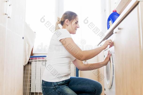 年幼的女人镶嵌和结尾的洗涤机器采用洗衣店房间