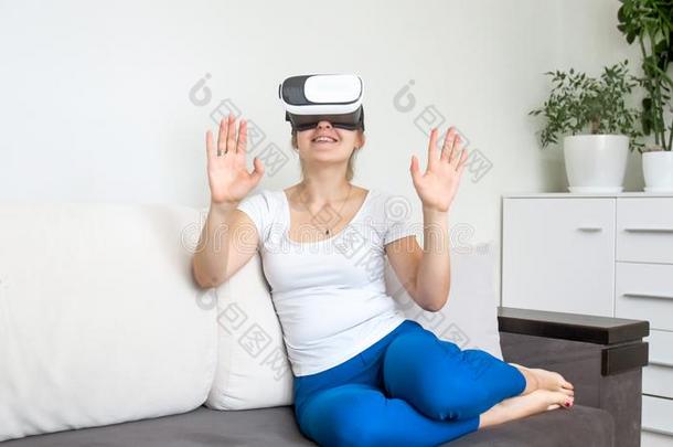 美丽的年幼的女人一次向沙发和使用VirtualReality虚拟现实戴在头上的耳机或听筒