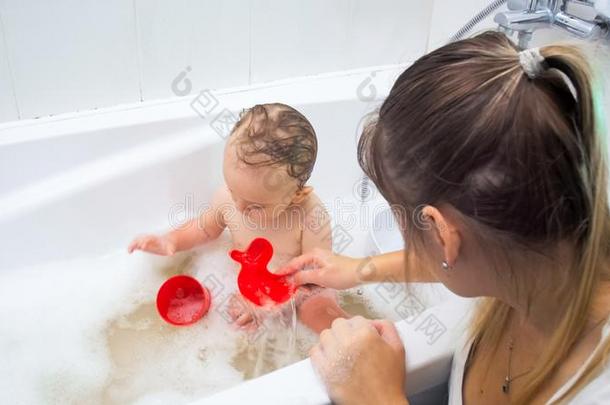 年幼的母亲演奏和她蹒跚行走的人儿子洗涤采用沐浴
