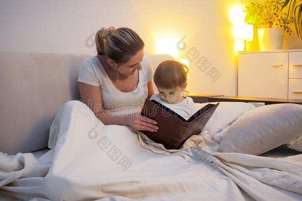 幸福的年幼的女人阅读故事向她向ddler儿子采用床在琢