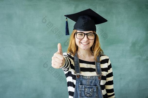 年幼的学生女孩展映拇指在上面向绿色的黑板