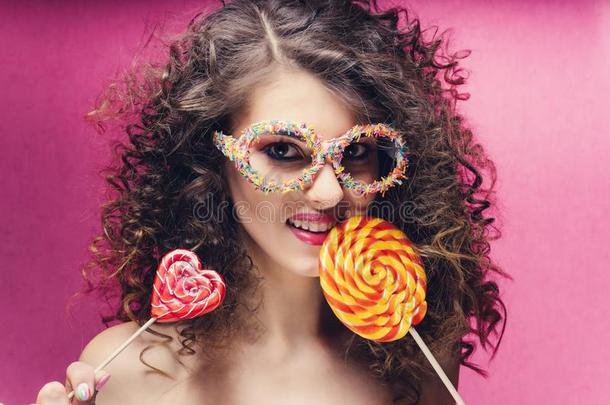 有卷发的美丽的女孩和红色的心棒棒糖采用糖果眼镜