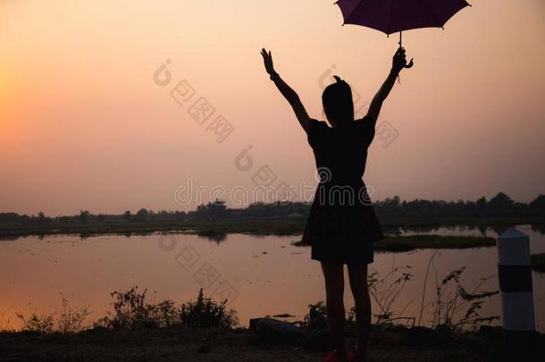 轮廓关于女儿增加一雨伞向天在日落在旁边湖