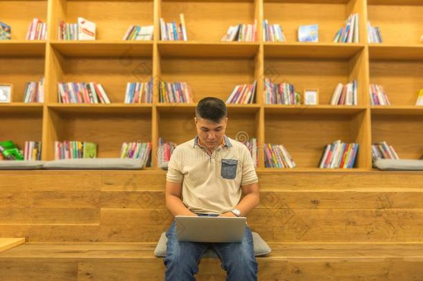 亚洲人学生使用便携式电脑在木制的图书馆书架后座