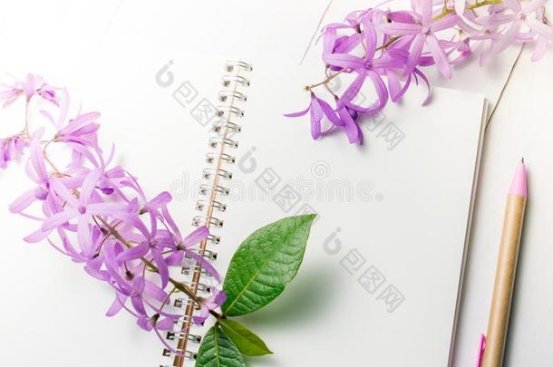 空白的笔记簿和笔和紫色的花向白色的木制的后面
