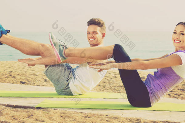 家伙和女孩在从事职业的瑜伽使摆姿势st和ing向海滩