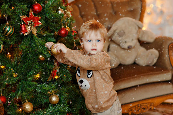 婴儿男孩白肤金发碧眼女人采用米黄色毛衣衣服在上面圣诞节树,悬挂
