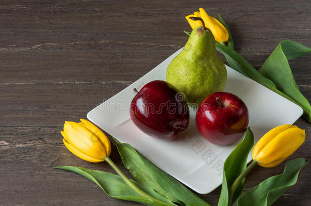 红色的苹果,绿色的梨和黄色的郁金香采用白色的盘子向灰色的