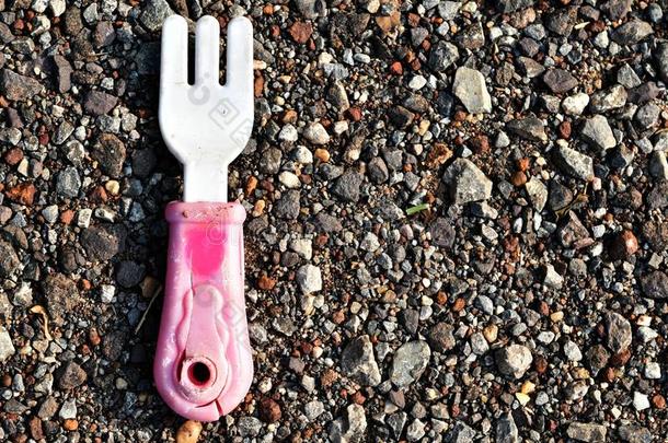 老的恶劣的粉红色的和白色的玩具塑料制品餐叉向恶劣的粗糙的地面