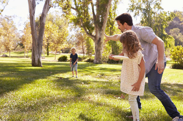 父亲和孩子们投掷运动飞盘采用公园同时