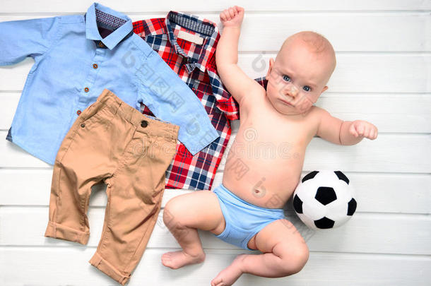 婴儿向白色的木制的背景和衣服和足球玩具.
