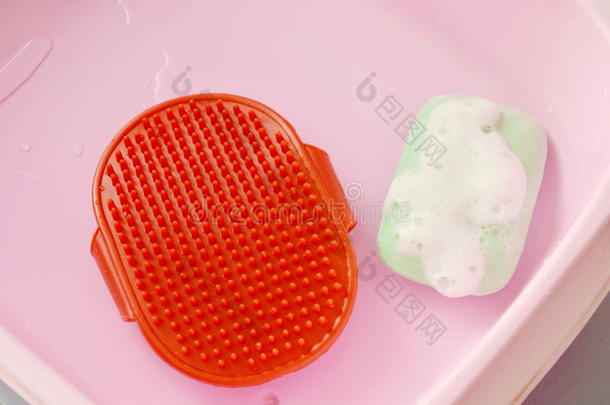 红色的橡胶狗沐浴刷子和宠物肥皂和泡向粉红色的塑料