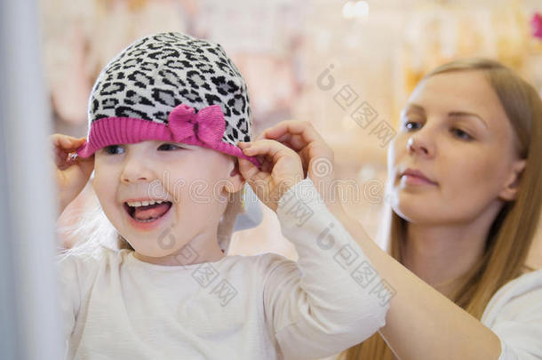小的幸福的女孩和妈咪做购物和购买粉红色的帽子