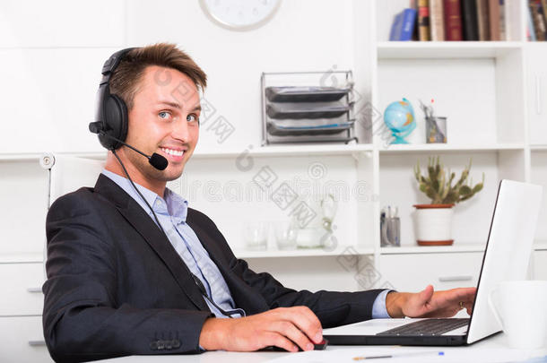 笑的成熟的男人讲话向戴在头上的耳机或听筒在办公室