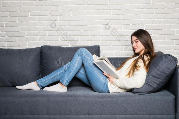 幸福的年幼的女人阅<strong>读故事</strong>书向长沙发椅在家