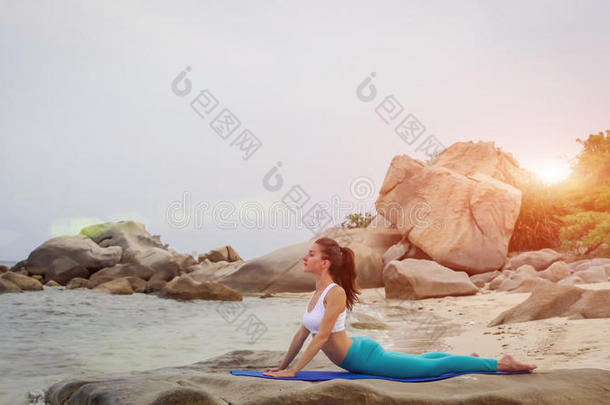 年幼的女人开业的瑜伽向指已提到的人海滩在日落.眼镜蛇使摆姿势