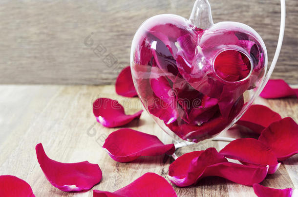 红色的玫瑰花瓣采用心装饰瓶向木制的背景