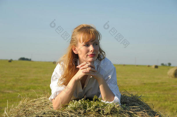 美丽的白肤金发碧眼女人国家女孩坐着向黄色的干草和束