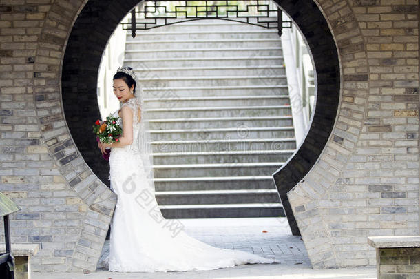 <strong>新娘</strong>拿住新婚的花束和白色的婚礼衣服在近处一砖