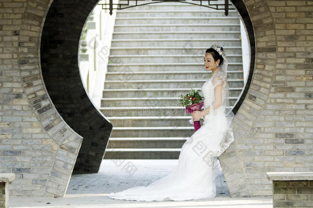 新娘拿住新婚的花束和白色的婚礼衣服在近处一砖