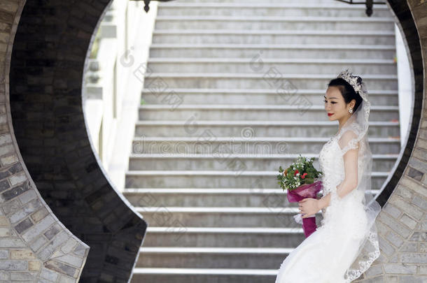 新娘拿住新婚的花束和白色的婚礼衣服在近处一砖