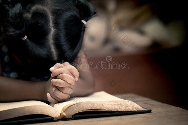 小的女孩手折叠的采用祈祷向一神圣的圣经