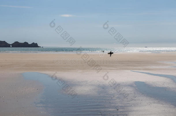 冲浪运动员步行越过宽的沙的夏海滩和海和多岩石的英语字母表的第3个字母