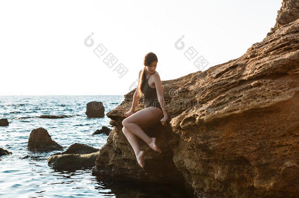 美丽的芭蕾舞女演员跳舞,使摆姿势向岩石在海滩,海后面