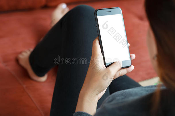 特写镜头女人使用聪明的电话可移动的白色的屏幕向沙发布置