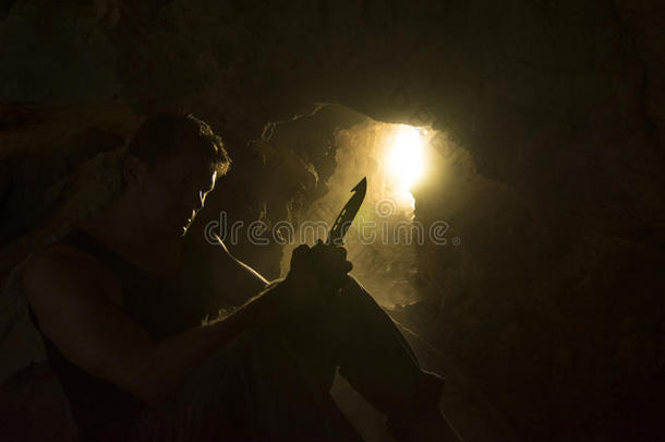 幸存男人和刀从背后照亮的采用布满灰尘的洞穴