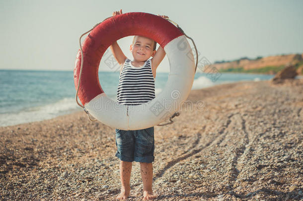 一男孩坐向指已提到的人海滩采用一有条纹的衬衫和一m一r采用e救生圈救生圈