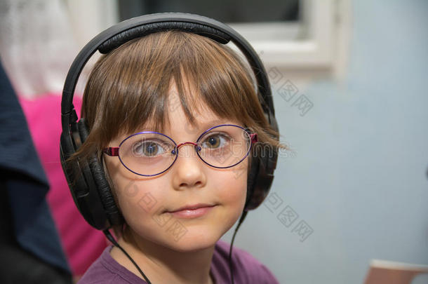 美丽的年幼的女孩收听的向音乐和戴在头上的耳机或听筒