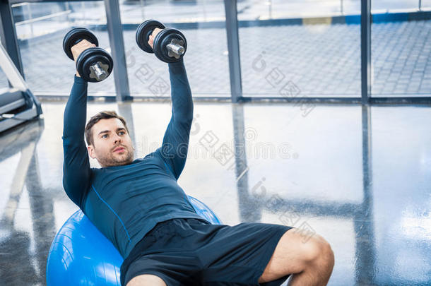 年幼的男人锻炼和哑铃向健康球在健身房