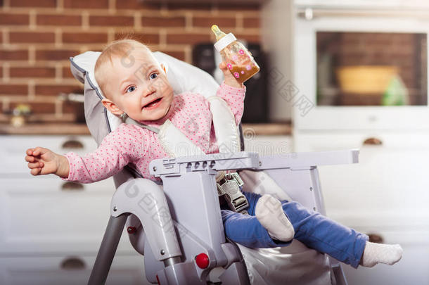 num.一年蹒跚行走的人女孩坐向婴儿高的椅子和给食瓶装