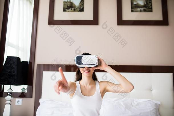 年幼的女人说谎向床,使用VirtualReality虚拟现实眼镜在家